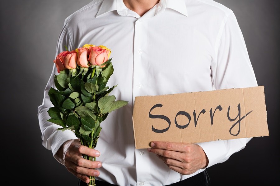 Man Holding Roses And Text Sorry Written On Cardboard Against Grey Background