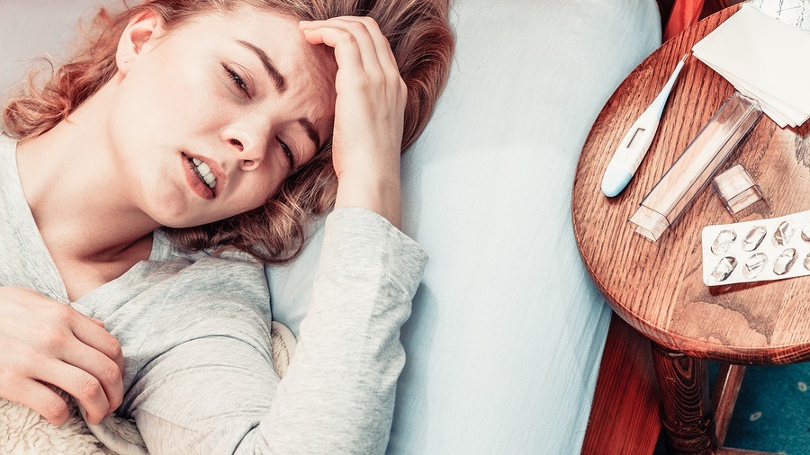 Sick woman suffering. Thermometer and pills on table.