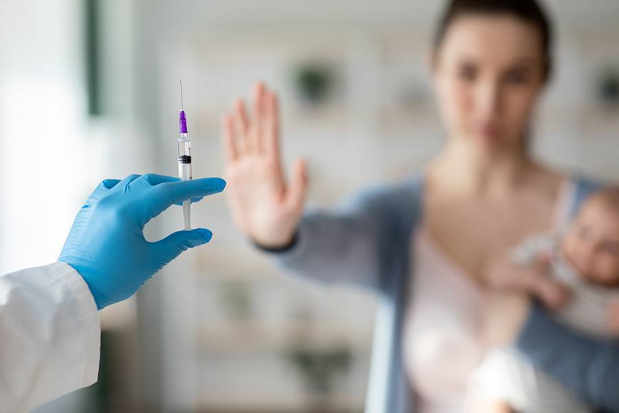 Vaccine Hesitancy. Woman With Newborn Baby Refusing Syringe In Doctors Hand